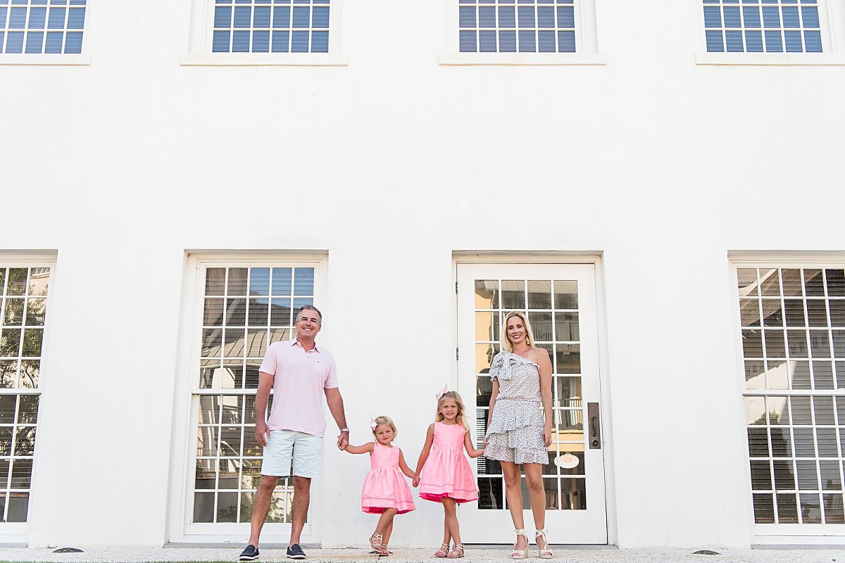 A family of four stands in front of the Rosemary Beach Town hall windows in a portrait session by Two Lights Photography