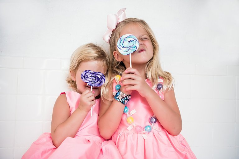 two sisters in pink dresses eating lollipops from the sugar shak at a family photography session by two lights photography